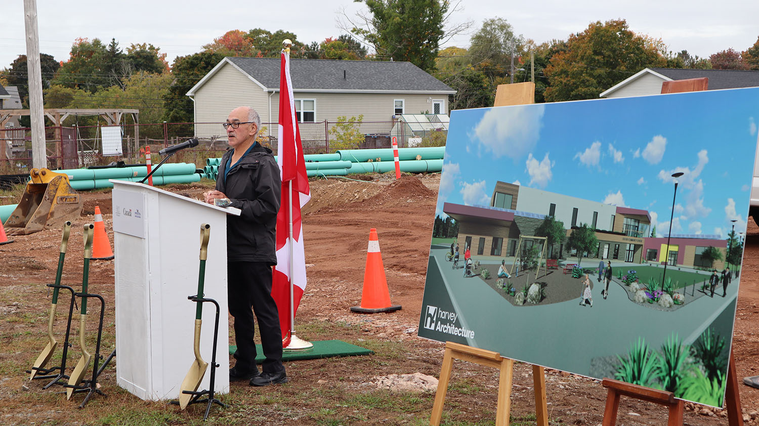 Elder Manson Gloade speaks at the podium beside a concept rendering of the new Oxford Community Centre.