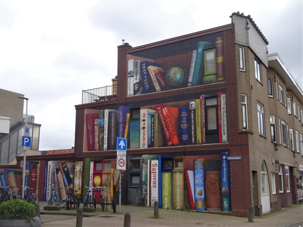 work in Utrecht by artists group Jan is de Man en Deef Feed, featuring a brick building where the wall is painted as bookshelves, with various books and objects.